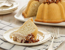 Load image into Gallery viewer, A slice of vanilla pound cake in the shape of a bundt filled with Italian buttercream and topped with toasted pecans. Serves 12. Oprah&#39;s Favorite Things. Packaged in our signature yellow and white striped gift box with a blue bow.